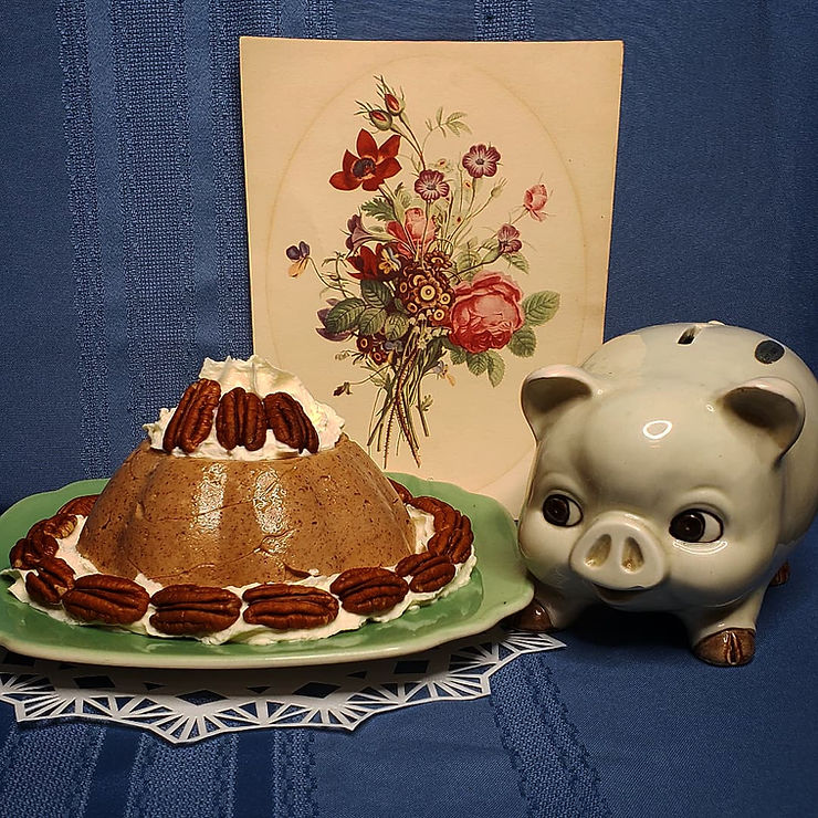A molded opaque brown pudding, garnished with whipped cream and whole pecans.