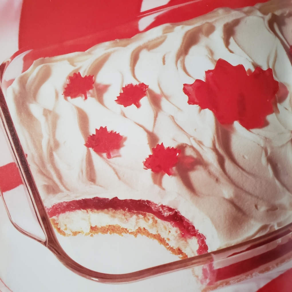 A layered bar-like dessert topped with whipped cream icing and little maple leaf jello cutouts